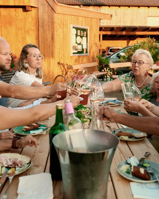 Familie und Freunde stoßen an einem Holztisch im Freien mit Essen in rustikaler Umgebung an